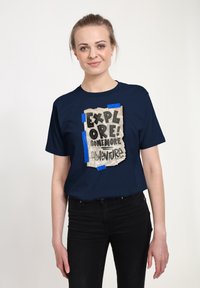 Námořnická modrá tričko s krátkým rukávem, na kterém je grafika zmuchlaného papíru s ručně psaným textem, připevněná modrou páskou, která přenáší poselství o dobrodružství.