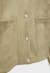Sammetsjacka i ljusbeige, med silverdetaljer, två framsidor fickor och en slät yta. Fokusera på knappstängningen och sömnaden.