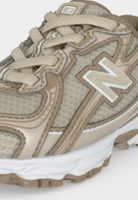 Μπεζ και λευκό παπούτσι τρεξίματος New Balance με υφασμάτινη υφή, παχιά σόλα και κορδόνια δεμένα μπροστά.