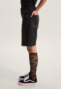 Falda de mezclilla negra con dobladillo deshilachado, combinada con calcetas negras con estampado hasta la rodilla y zapatillas negras con suelas rosas y detalles blancos.