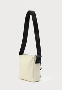 Õlakott pehmest beežist kangast, millel on must reguleeritav rihm ja tõmblukuga sulgemine. Ruudukujuline minimaliseeritud disainiga.