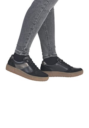Black sneaker with contrasting grey accents and a textured, brown rubber sole. Features laces and a side zip, displayed on a person in grey jeans.