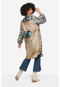 Kimono lungo e decorato con maniche bianche e nere. Presenta una grande grafica a forma di occhio su uno sfondo beige, arricchita da accenti colorati.