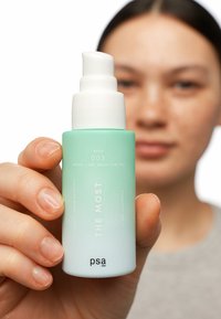 Hydrating serumflaska i mintgradient med vit pump, märkt "THE MOST," med stegnummer "003" och varumärket "psa" på basen.