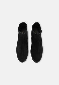 Botines de ante negros con una textura suave, diseño minimalista y paneles laterales elásticos. Cuentan con una suela de goma negra.