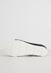 Semelle de chaussure noire avec une semelle extérieure en caoutchouc blanche épaisse et segmentée, taille 37 marquée au centre, photographiée sur fond gris clair.
