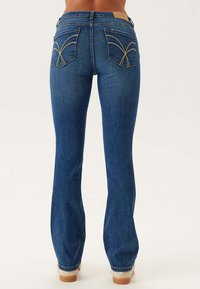 Uppfläkt blå denimjeans med medelhög midja, kontrasterande sömmar och dekorativa bakfickor med unika broderade mönster.