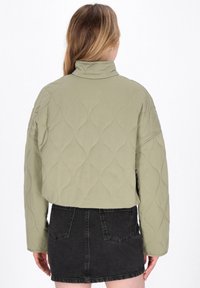 Quiltet olivengrøn jakke med høj krave, prydet med bølgede stikninger; parret med en sort denimnederdel.