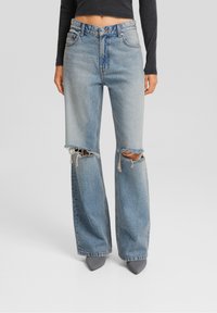 Light blue high-waisted jeans with wide legs, featuring large frayed knee rips. Made from denim, the texture is soft with a faded wash.