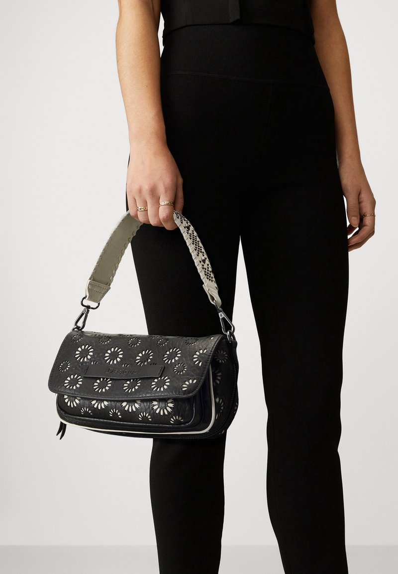 Borsa a tracolla in pelle nera con design a fiori intagliato, dotata di una tracolla a fantasia contrastante. Finitura testurizzata e chiusura a pattina magnetica.