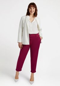 Biała marynarka na białej koszuli z guzikami i bordowych spodenka cropped. Modelka ma na sobie beżowe szpilki, prezentując swobodny, ale elegancki wygląd.