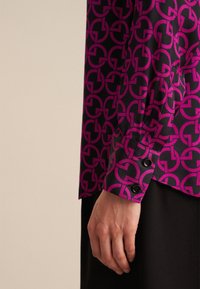 Camicia a maniche lunghe in satin nero con un motivo circolare magenta ripetuto, dotata di polsini con bottoni e design aderente.