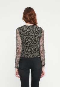 Sheer long-sleeve top featuring a black and tan zebra stripe pattern, a rounded neckline, and a fitted design. Worn with black jeans.