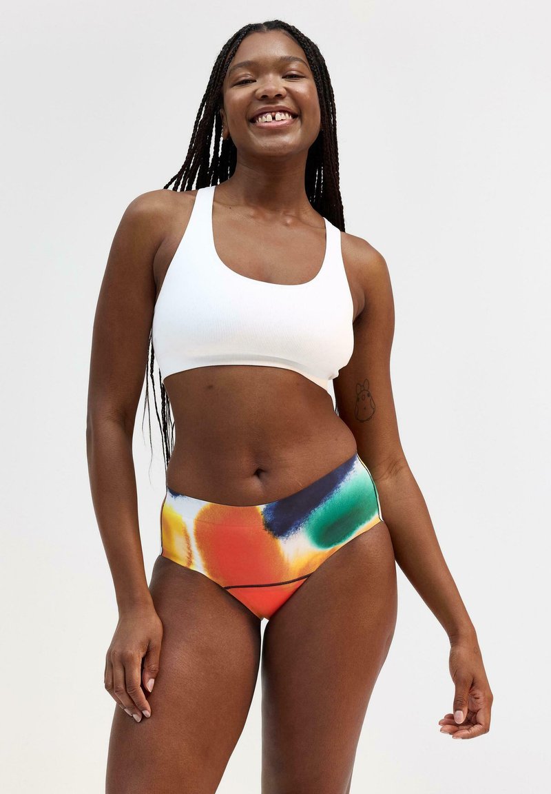 Hvid ribbet cropped top sat sammen med højhalsede bikiniunderdele med et farverigt abstrakt mønster i orange, blå, grøn og gul.