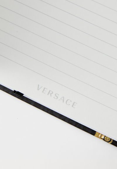 Quaderno nero con pagine a righe, con il logo "VERSACE" in rilievo, bordi testurizzati e dettagli decorativi con motivo sulla rilegatura.