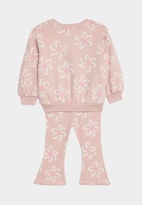 Różowy dres z kwiatowym wzorem, ozdobiony białymi stokrotkami z różowymi środkami. Bluzka ma fason zakładany przez głowę, a spodnie posiadają żebrowaną teksturę i zwiewne mankiety.