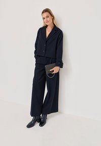 Un costume rayé marine comprenant un blazer court avec boutons et un pantalon large taille haute, associé à des bottines noires brillantes et un sac à main.