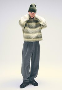 Zielona czapka beanie, oversize'owy futrzany sweter z kremowymi paskami oraz szare szerokie spodnie. Brązowe sneakersy dopełniają outfit.