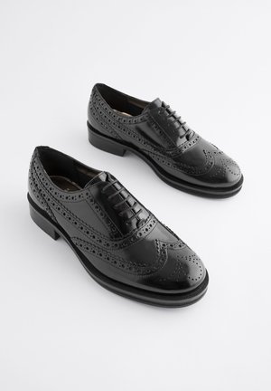 Pantofi brogue negri din piele cu detalii perforate, vârf rotund și design cu șireturi. Prezintă un toc jos stratificat și un finisaj neted.