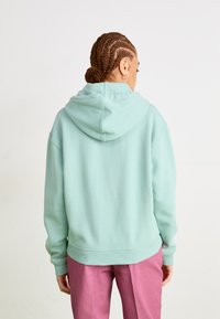 Sweatshirt verde menta com capuz, feito de um tecido suave, apresentando um corte descontraído, punhos em ribana e calças cor de rosa combinantes.
