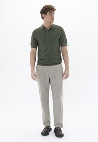 Cămașă polo verde cu mânecă scurtă, cu un model texturat, asortată cu pantaloni bej deschis, plisati și pantofi maro închis.