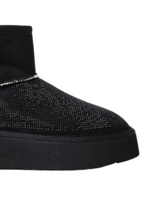 Stivale alla caviglia nero con tomaia in rete testurizzata, dotato di una suola nera spessa e solida. Nessun hardware o decorazione visibile.