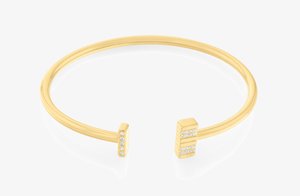 Kuldtooni metallist käevõru, millel on sile viimistlus ja kaks ruudukujulist otsa, millest igaüks on kaunistatud väikeste selgete kristallide rida.