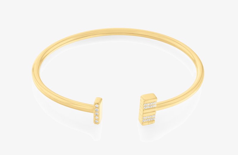 Kuldtooni metallist käevõru, millel on sile viimistlus ja kaks ruudukujulist otsa, millest igaüks on kaunistatud väikeste selgete kristallide rida.