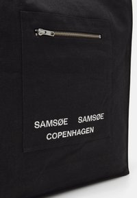 Black canvas tote bag featuring a front zippered pocket. "SAMSEØ SAMSEØ COPENHAGEN" embossed in white text on the front.
