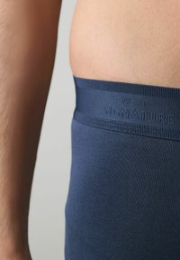 Mörkblå stretchtygsboxershorts med ett mjukt midjeband som har präglad text "NEXT" och "SIGNATURE". Närbild på midjan.