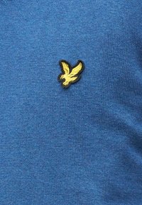 Kék kötött pulóver puha textúrával, bal mellrészen sárga hímzett madár logó fekete szegéllyel.