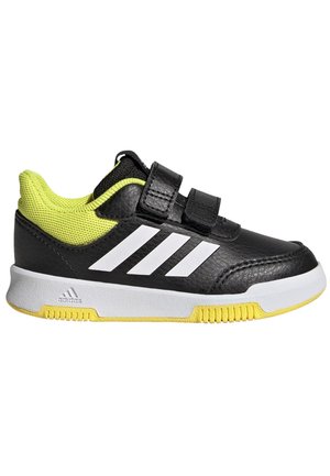 Zapatilla deportiva negra con parte superior de cuero sintético y malla, diseño de tres rayas en blanco, acentos amarillos y correas de Velcro para un ajuste seguro.