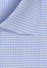 Blauw en wit patroonstof met een zigzagontwerp en een gestructureerd oppervlak. Zichtbare stiksels langs de randen en scherpe hoekdetails.