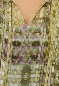 V-Ausschnitt Bluse mit grünem und lila Batikmuster, die vertikale Falten und subtile goldene Akzente im gesamten Stoff aufweist.
