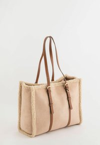 Bolso tote de ante beige con ribete de piel clara; cuenta con dos correas de cuero marrón y dos detalles de cuero marrón, forma rectangular y textura suave.