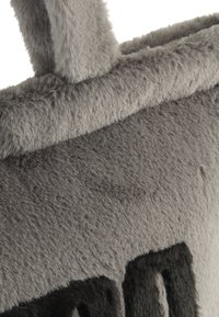 Contenitore plush grigio con una texture morbida e pelosa, caratterizzato da una forma arrotondata e un manico grigio prominente. Accenti neri visibili sul lato.
