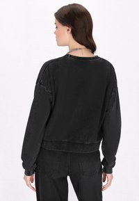 Felpa nera oversize con una consistenza morbida, polsini a costine e scollo rotondo. Presenta una vestibilità comoda e una leggera lucentezza.