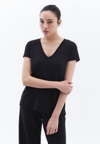 T-shirt nero a V realizzato in tessuto morbido e elasticizzato; maniche corte e vestibilità comoda, abbinato a pantaloni neri.