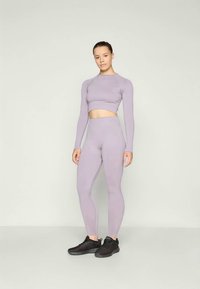 Lilac long-sleeve crop top and high-waisted leggings set, made of stretchy fabric, with a smooth texture and fitted design. Black sneakers.