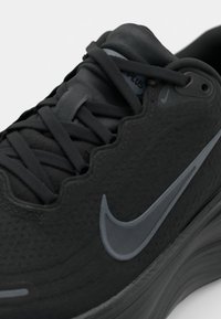 Basket noire avec tige texturée, design en vague et semelle arrondie. Comprend des accents gris et un logo, avec plusieurs lacets noirs.