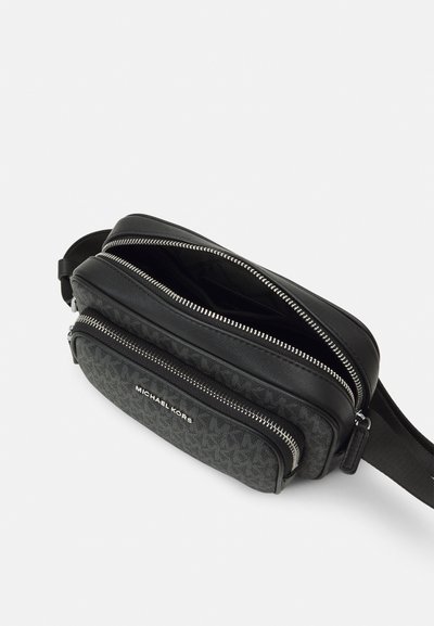 Sac à bandoulière noir avec de multiples compartiments zippés, un extérieur texturé avec un motif monogramme, et un détail logo sur le devant.