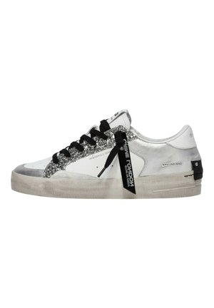 Sneaker bianca basse con dettagli glitter argento, lacci neri, etichetta nera con marchio e suola beige leggermente consumata.