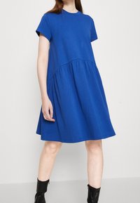 Blå bomullsklänning med korta ärmar, rund halsringning och en lagerdesign. Har en figurnära bodice och en utsvängd kjol.