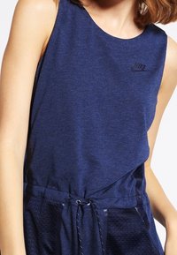 Sleeveless navy blue athletic top made of soft fabric. Features a round neckline and a drawstring waistband. Small logo detail on front.