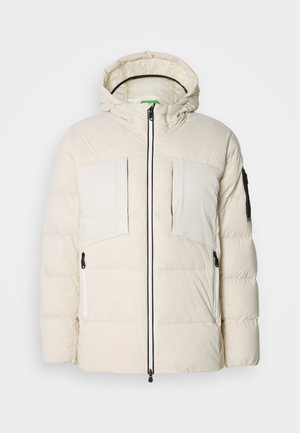 Chaqueta de plumas en beige claro con capucha, que cuenta con dos bolsillos en el pecho, dos cremalleras laterales y un detalle negro en la manga. Textura suave.