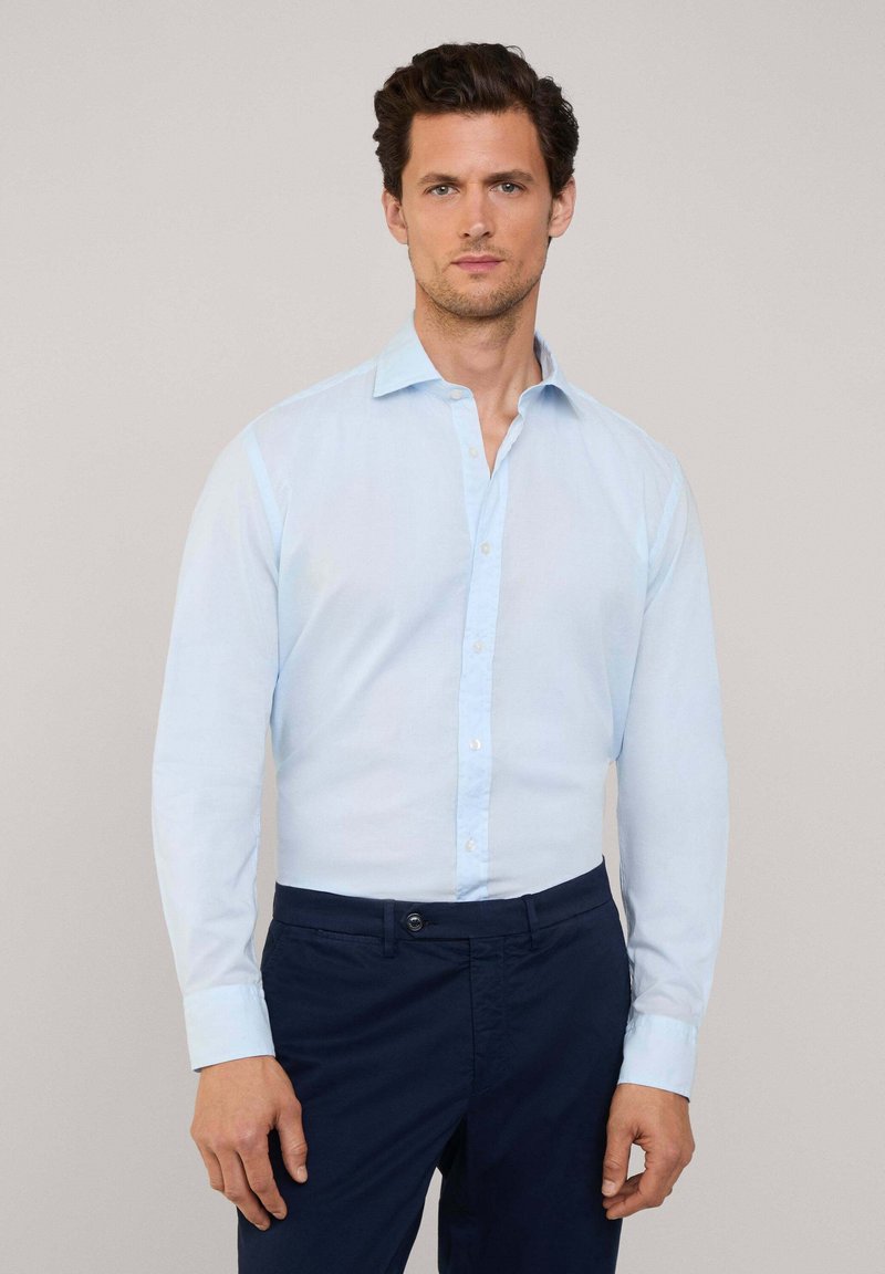 Camisa abotonada de color azul claro con mangas largas, diseño con cuello y textura de tela suave, combinada con pantalones oscuros de color navy.