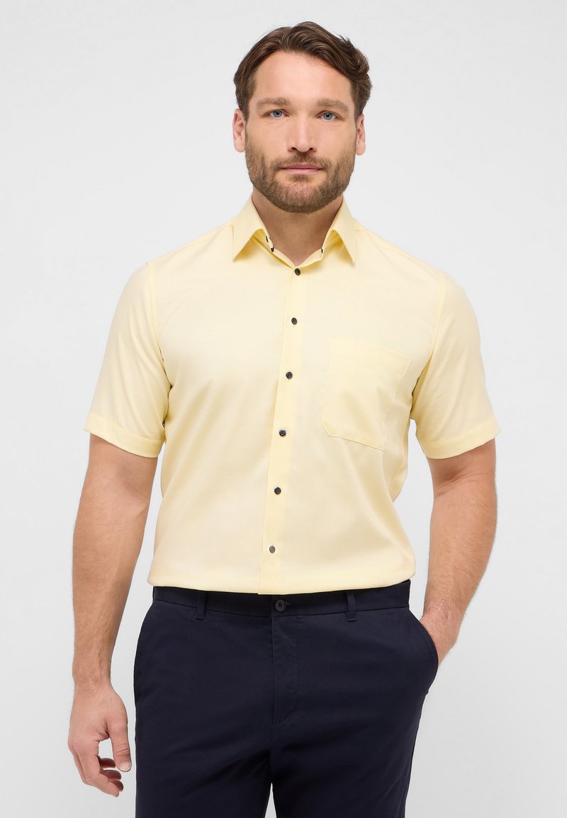 Camicia a maniche corte con colletto in tessuto giallo chiaro con una sottile texture, dotata di taschino sul petto e dettagli con bottoni neri.