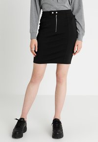 Černá mini sukně s úzkým střihem, zapínáním na zip vpředu a dvěma ozdobnými knoflíky. Kombinována se šedou mikinou a černými teniskami.