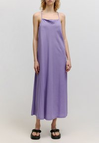 Lila Maxikleid aus leichtem Stoff, mit dünnen Trägern, einem Cowl-Ausschnitt und einer lockeren Silhouette. Getragen mit schwarzen Plateausandalen.