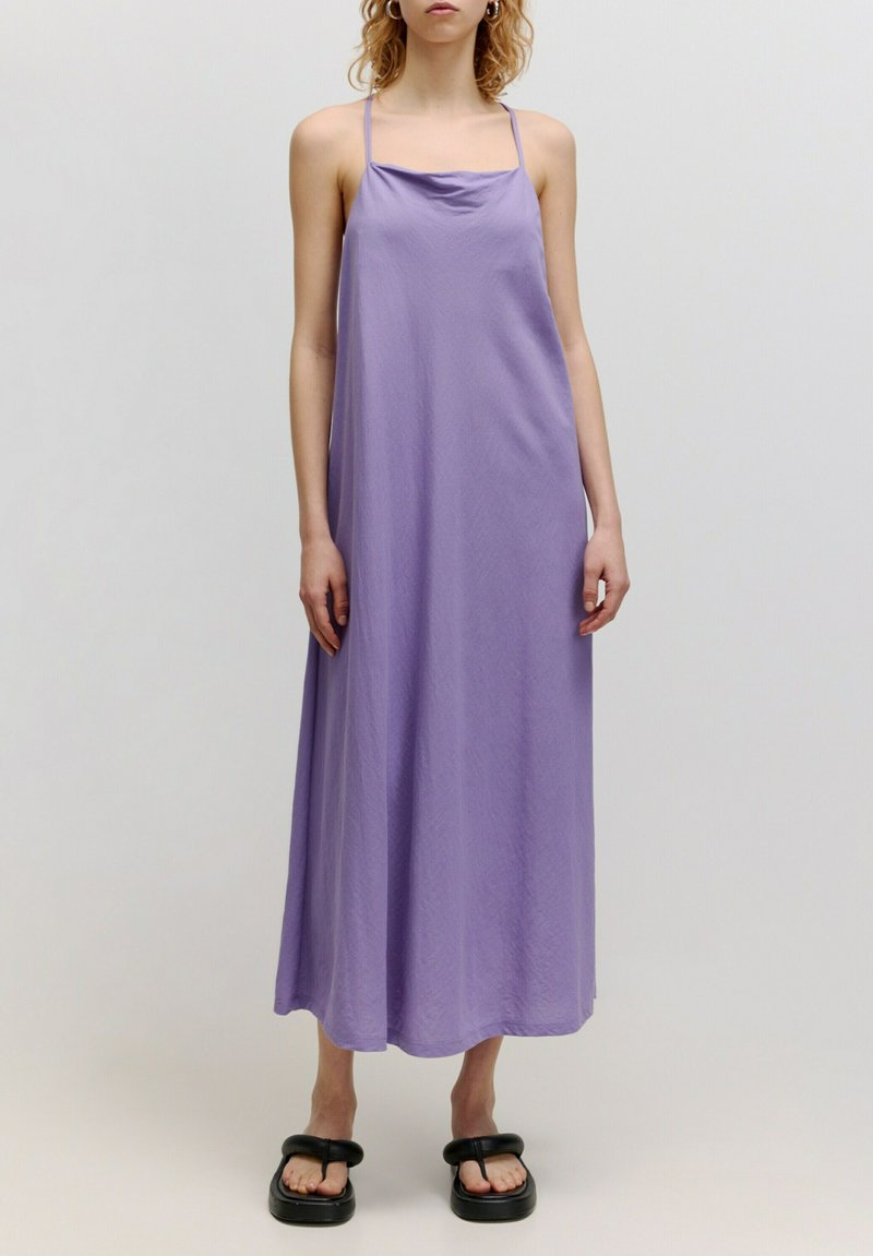 Lila Maxikleid aus leichtem Stoff, mit dünnen Trägern, einem Cowl-Ausschnitt und einer lockeren Silhouette. Getragen mit schwarzen Plateausandalen.